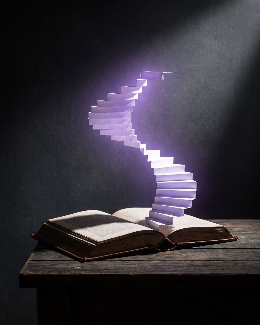 Livro aberto do qual sobe uma escada de papel iluminada